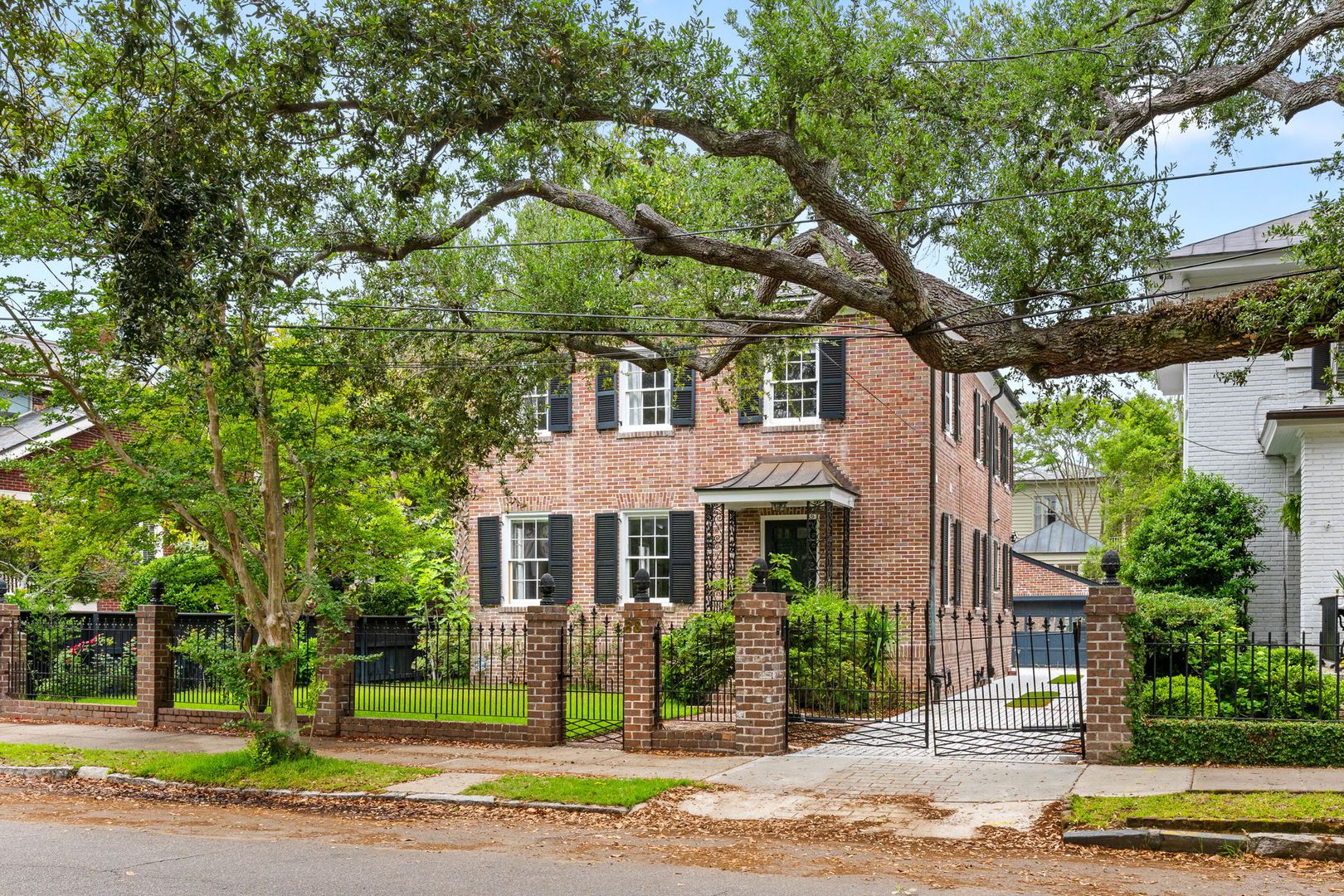 Brick home with black shutters behind an iron fence under live oaks, South of Broad, Charleston